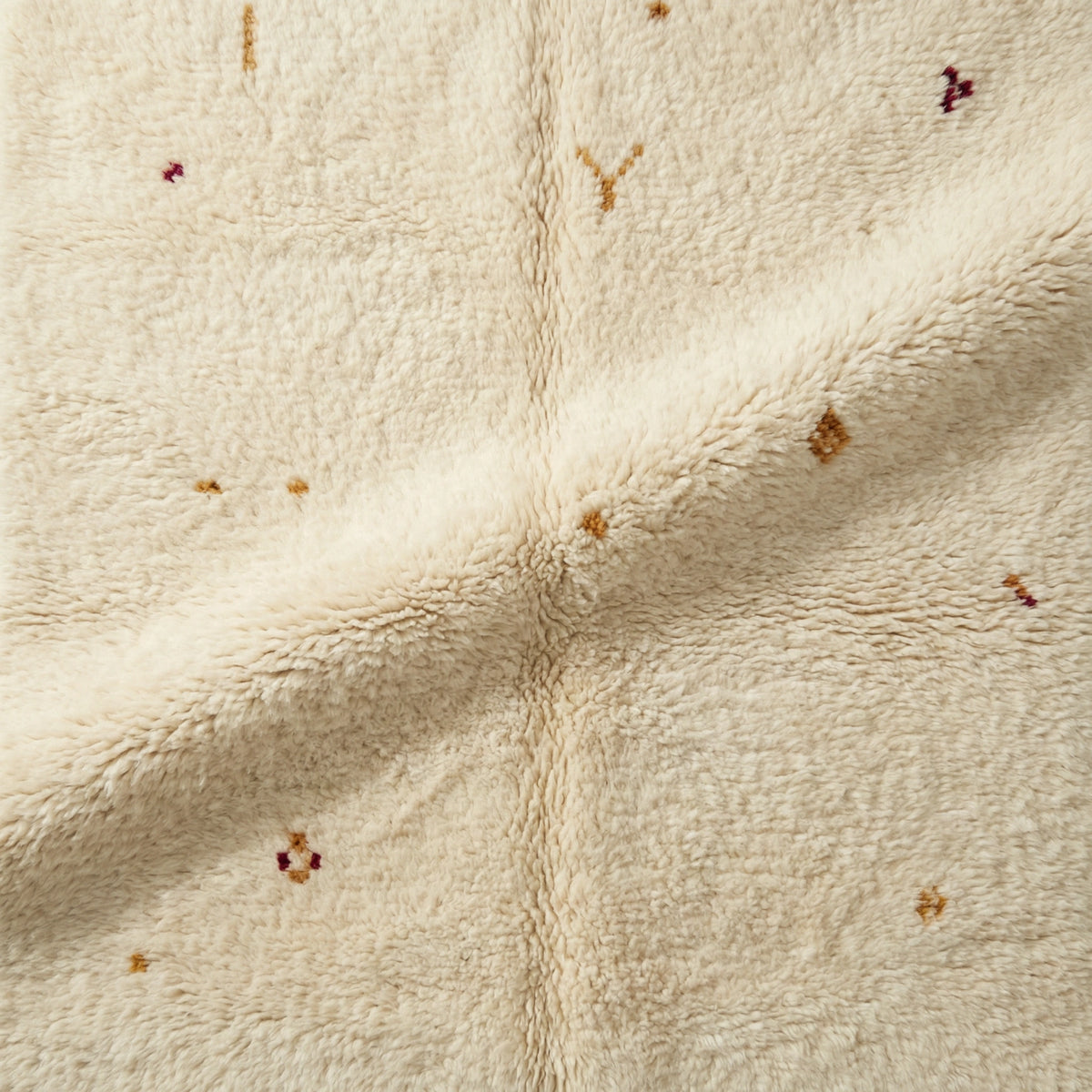 Detail of Moroccan wool rug, small yellow, orange and red motifs on a cream wool ground